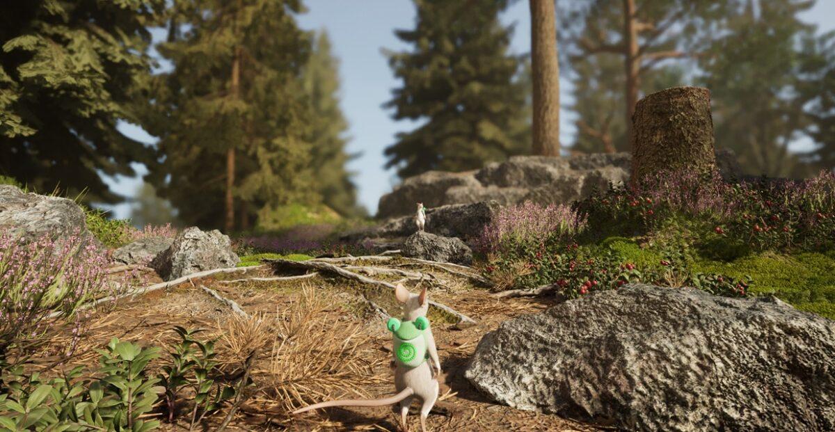 Die kleine Maus von Hela steht vor einer waldigen Umgebung. Auf dem Rücken strägt sie einen grünen Rucksack